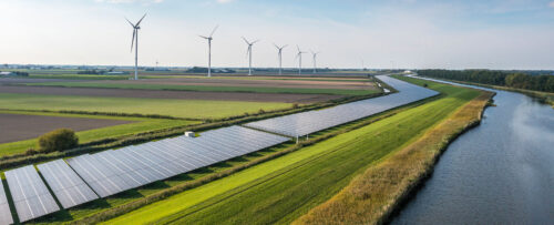 solar panels along river with wind turbines in background
